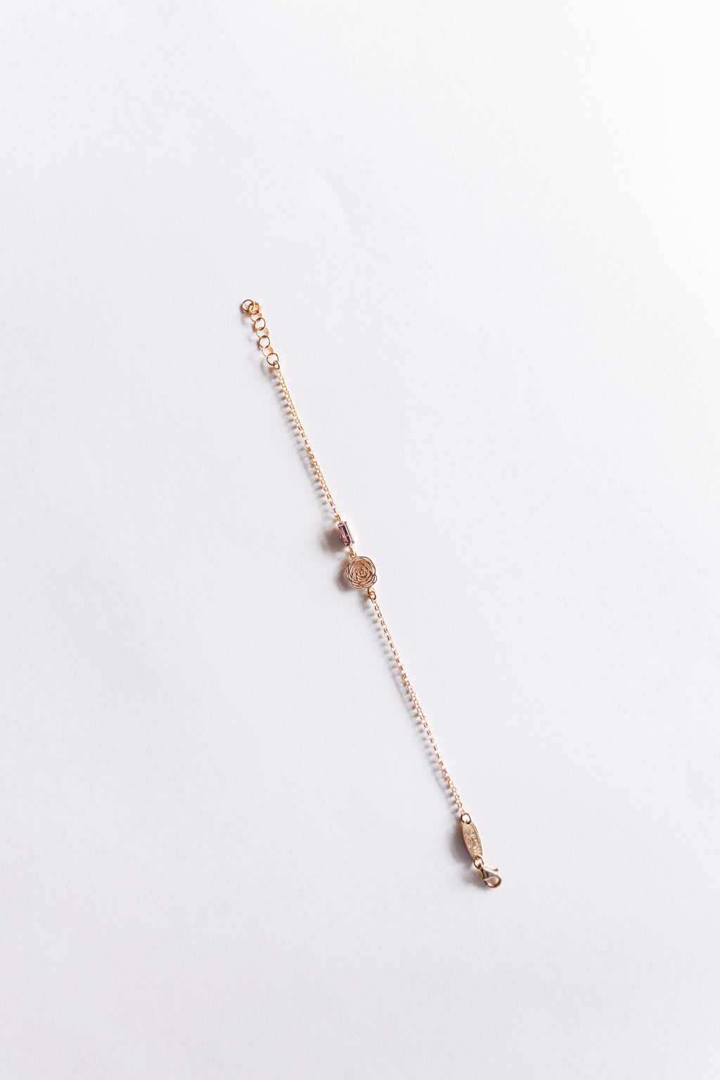 A rose gold-colored sterling silver bracelet with rose design and crystal laid out on a white surface.
