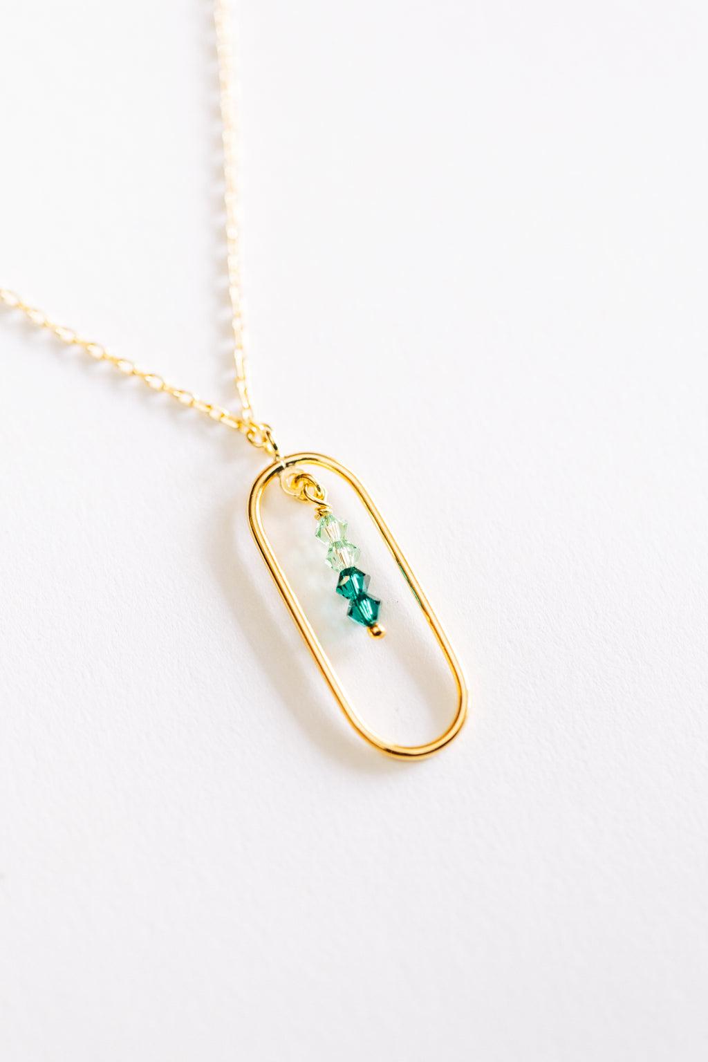 A hypoallergenic gold-colored necklace with a small pendant featuring green crystals on a white background