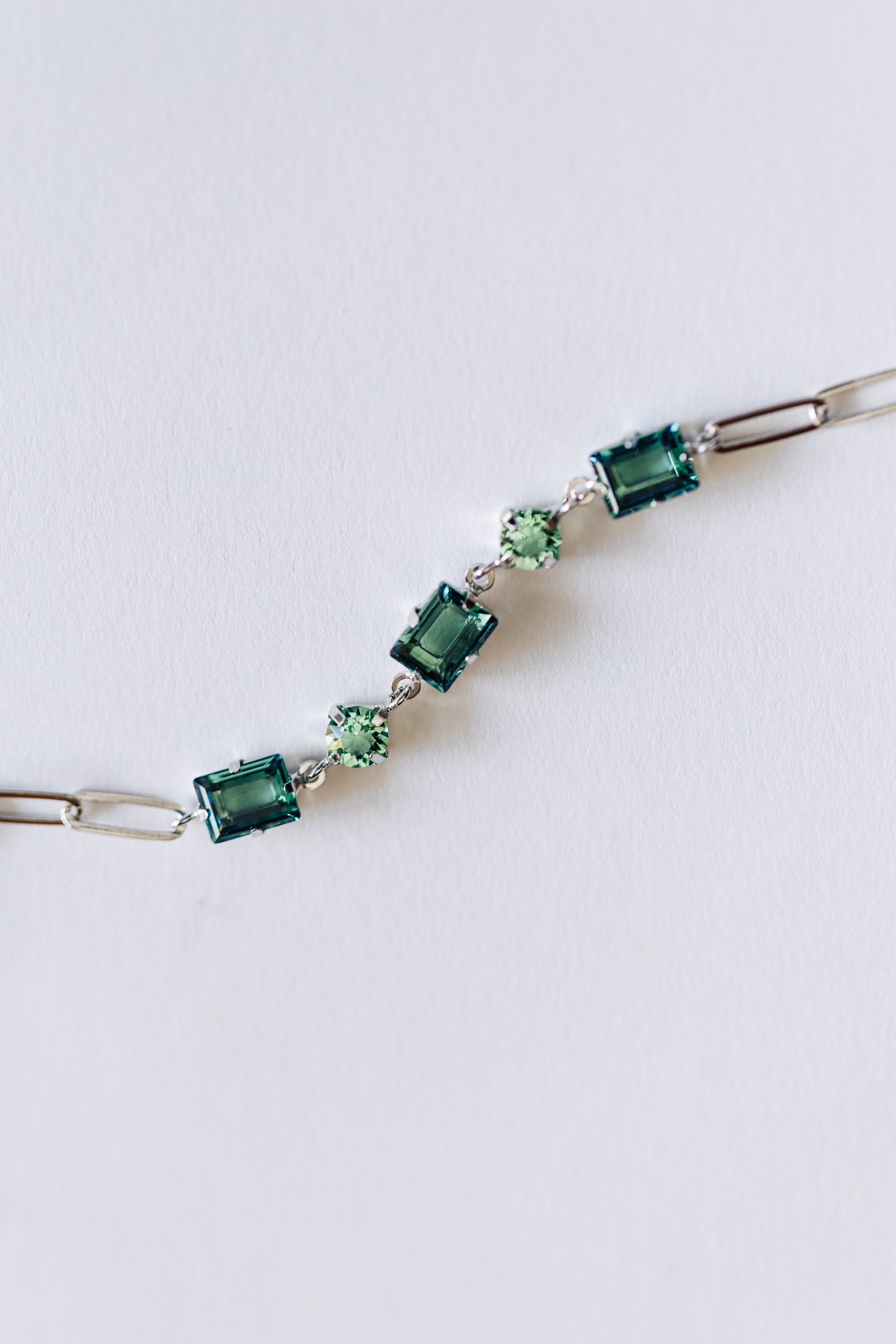 A silver bracelet with green crystals and silver accents, displayed against a white background.