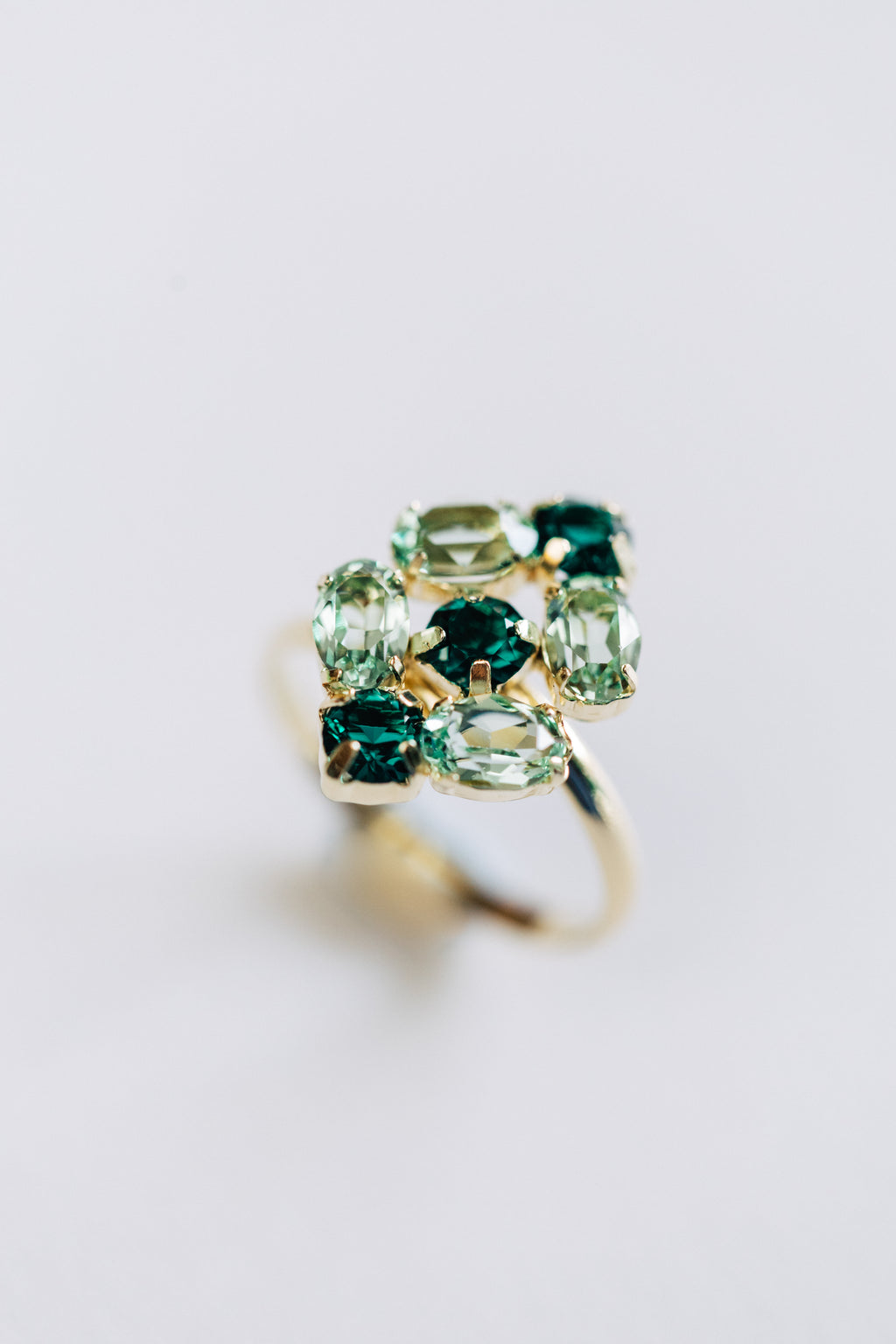 A hypoallergenic gold ring with multiple green gemstones arranged in a cluster design.