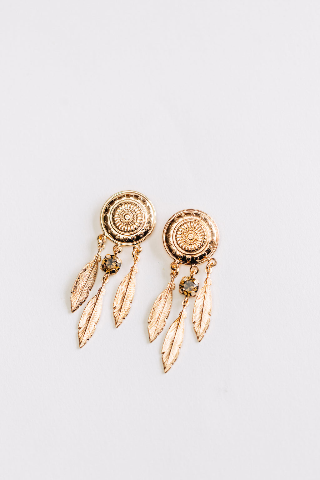 A pair of rose gold hypoallergenic earrings with intricate details and small crystal embellishments, featuring talisman and feather design.