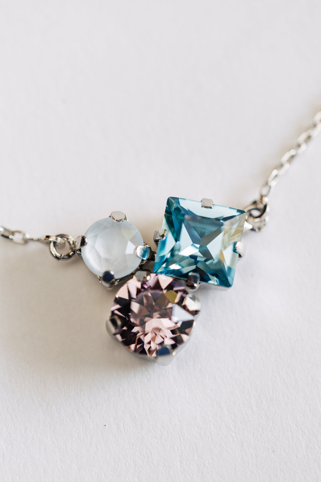 A hypoallergenic silver necklace with three multicolored crystals on a white background.