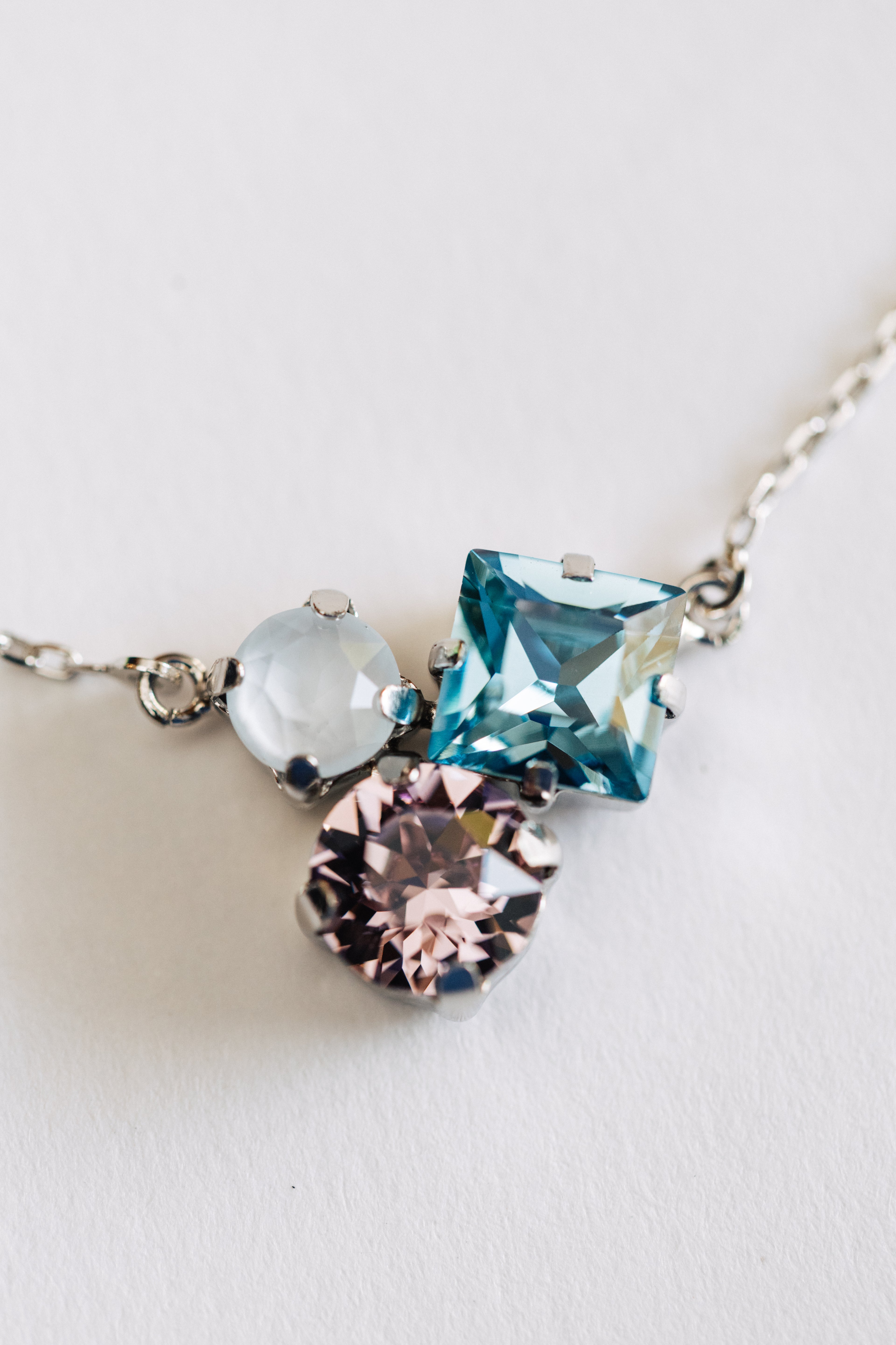A silver necklace with three multicolored crystals on a white background.