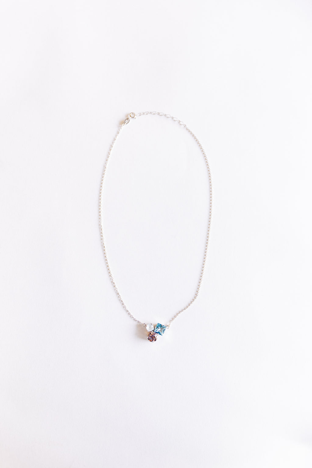 A silver necklace with a three-stone pendant on a white background.