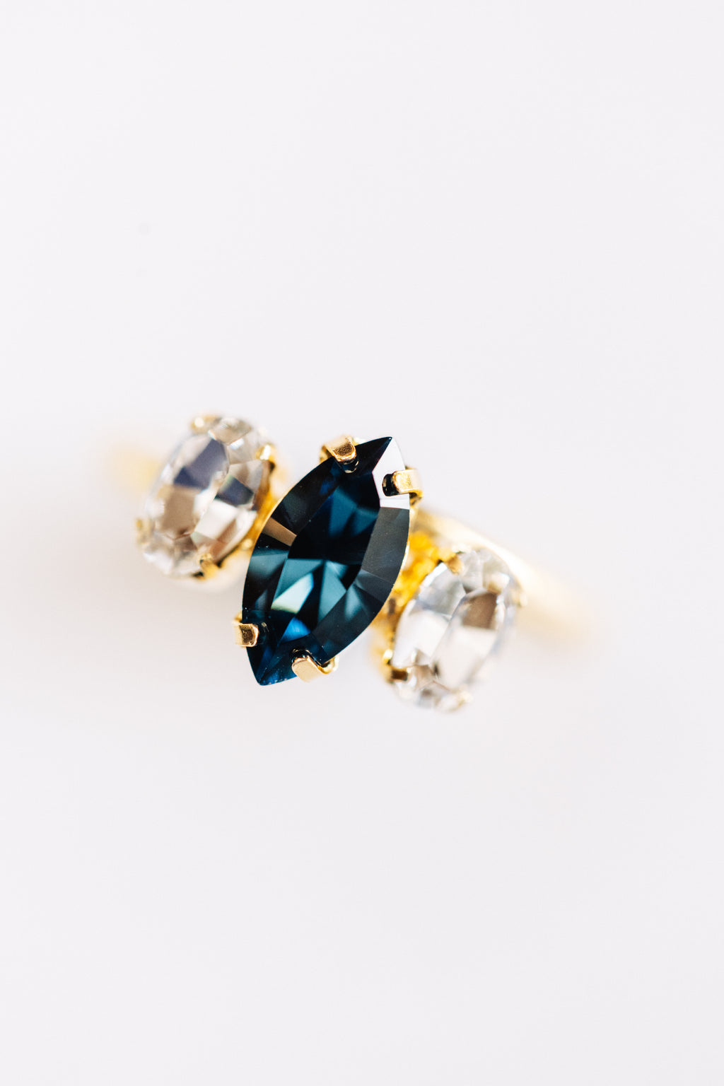 A hypoallergenic gold-colored ring with a large blue center stone and smaller clear stones on the sides.