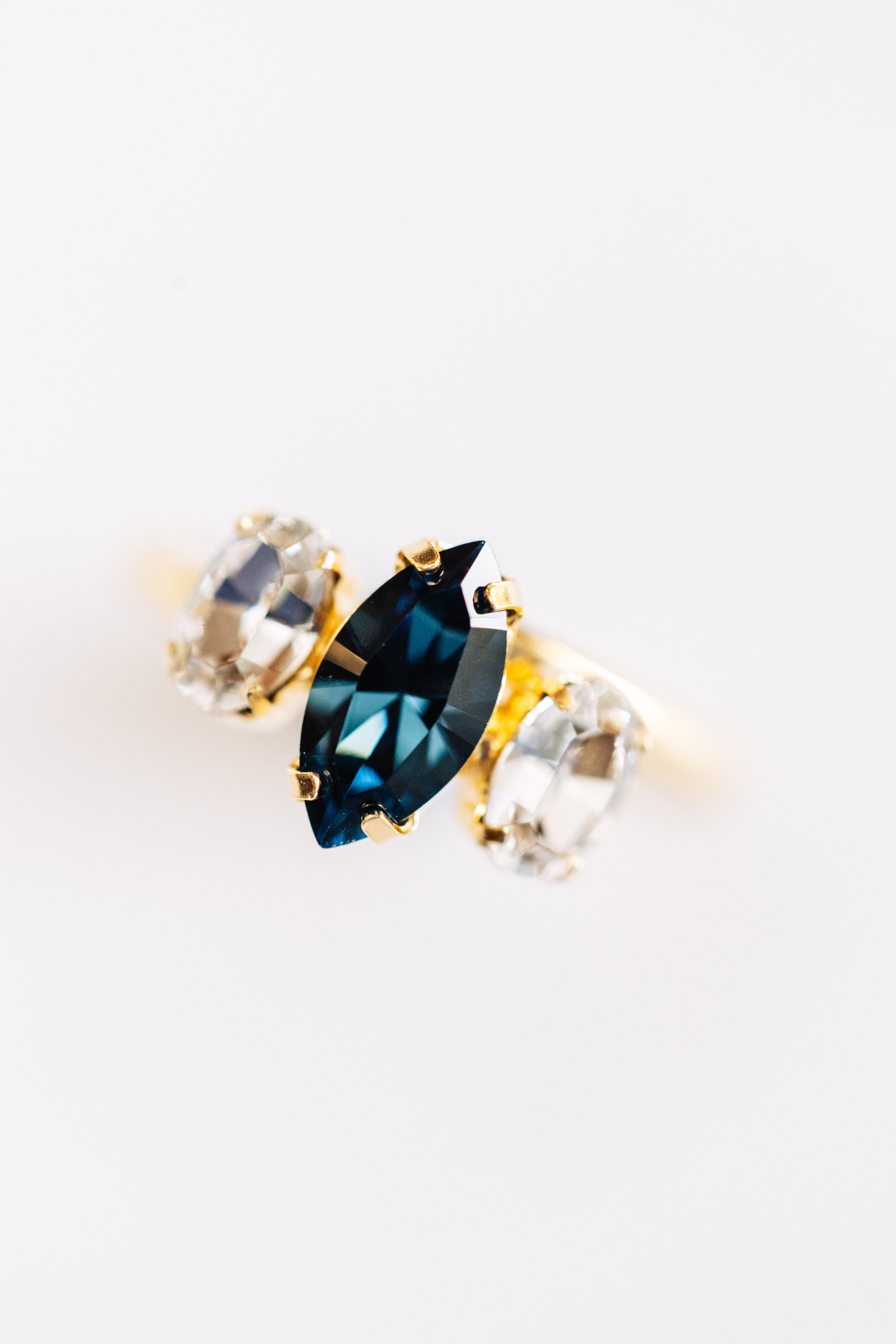 A gold-colored ring with a large blue center stone and smaller clear stones on the sides.